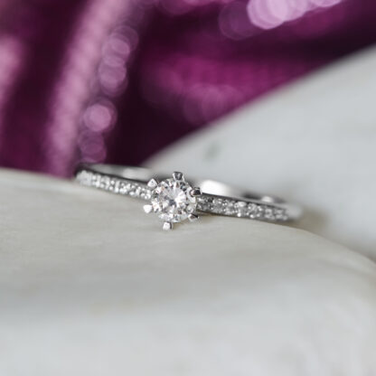 Solitär Ring aus Gold mit einem Diamanten und weiteren Brillanten auf der Ringschiene.